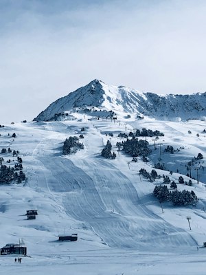 Groomed pistes and chairlifts below a rocky snow-plastered peak with scattered pines at Baqueira