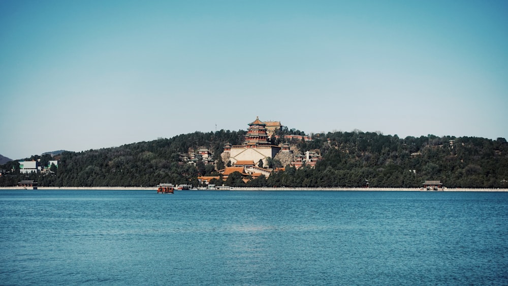 houses and buildings surrounded with tall and green trees near body of water under blue and white sky during daytime