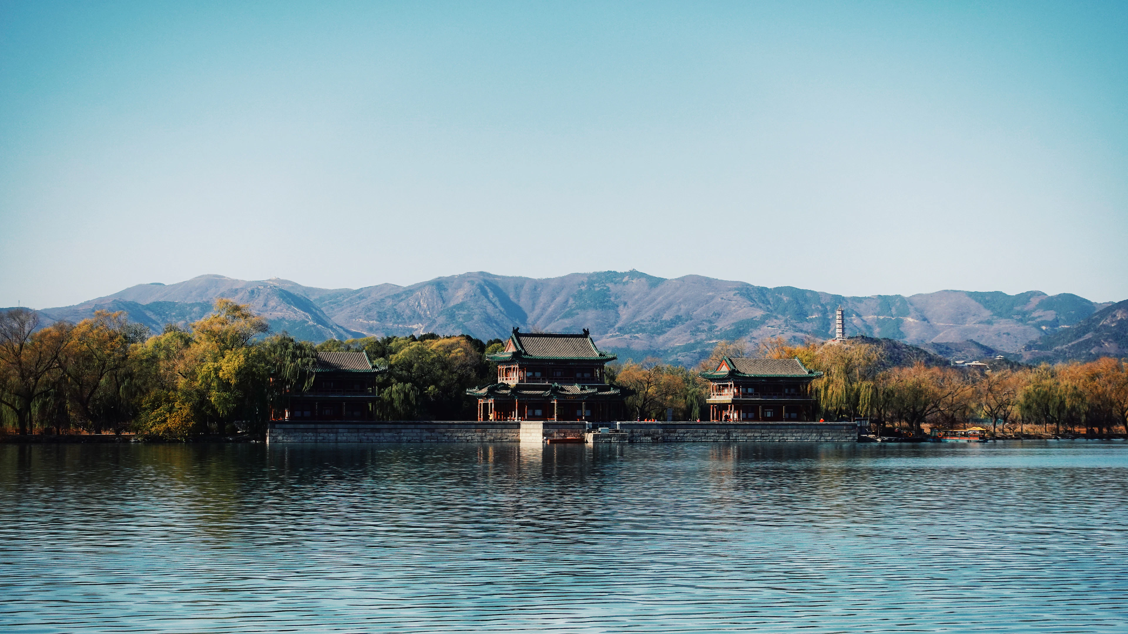 Lakeside pavilions of the Summer Palace sit at the water's edge with distant mountains and autumn trees behind.