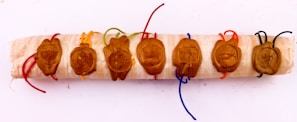 A series of seven wax seals, each embossed with different symbols, are attached to a wooden scroll. The seals are connected by colorful strings, including red, orange, green, blue, and black. The symbols on the seals include a menorah, grapes, a crown, a Star of David, a fish, and other intricate designs.