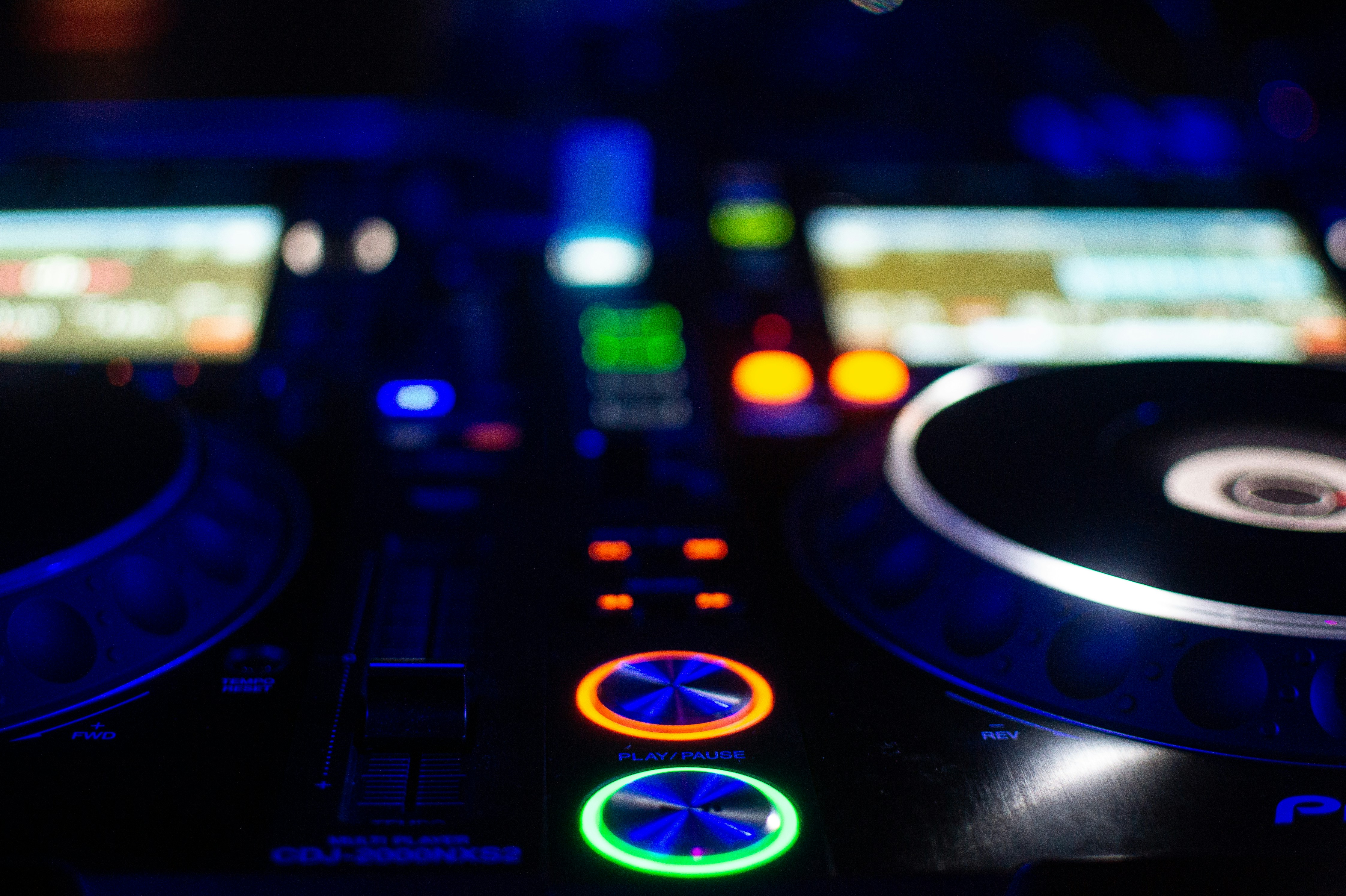 A close-up view of a DJ mixer with colorful LED lights illuminating the control buttons and components. The scene is set in a dimly lit environment, highlighting the vibrant colors on the mixer.