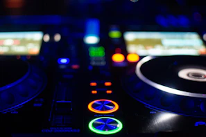 Close-up of a DJ mixing console with colorful LED lights glowing in a dark club setting.