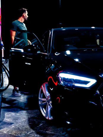 A professional chauffeur opening the door of a polished black car under the neon lights of the Las Vegas Strip.