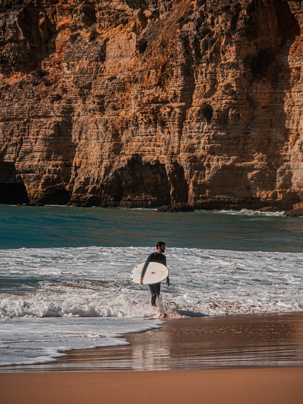 man holding surfboard walking on seashore