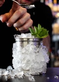 Hands expertly pouring mocktail ingredients into a glass garnished with mint leaves