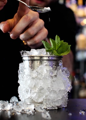 Hands expertly pouring mocktail ingredients into a glass garnished with mint leaves