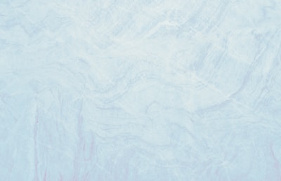 A marble texture with a smooth and subtle mix of light blue and white tones. The surface pattern consists of delicate, swirling veins and slight variations in color, resembling natural stone.