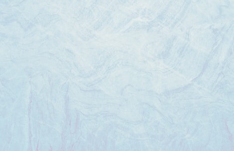 A marble texture with a smooth and subtle mix of light blue and white tones. The surface pattern consists of delicate, swirling veins and slight variations in color, resembling natural stone.