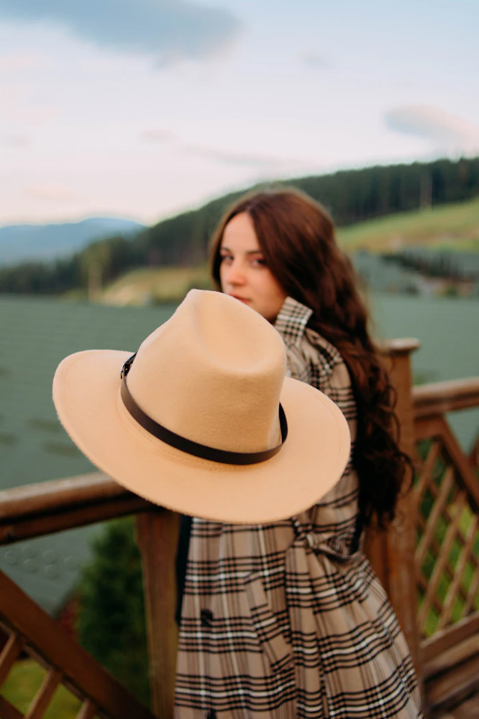 Woman in a plaid coat holding a hat by a wooden rail