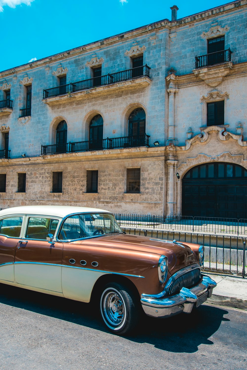 carro marrom e branco estacionado em frente ao edifício de concreto branco