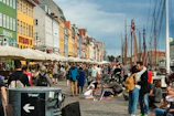 a crowd of people walking around a harbor next to tall buildings