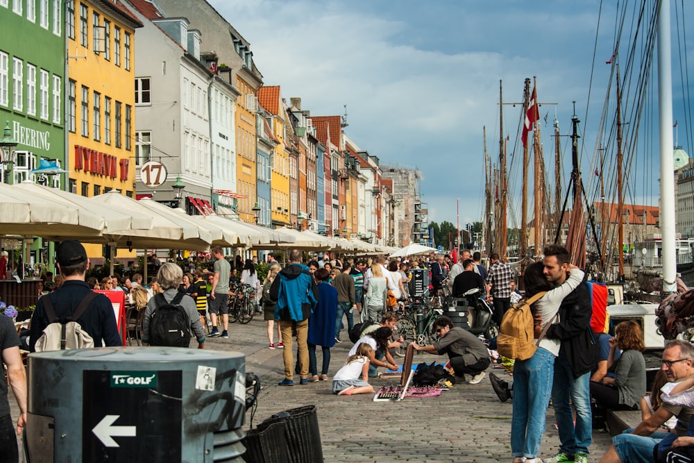 a crowd of people walking around a harbor next to tall buildings