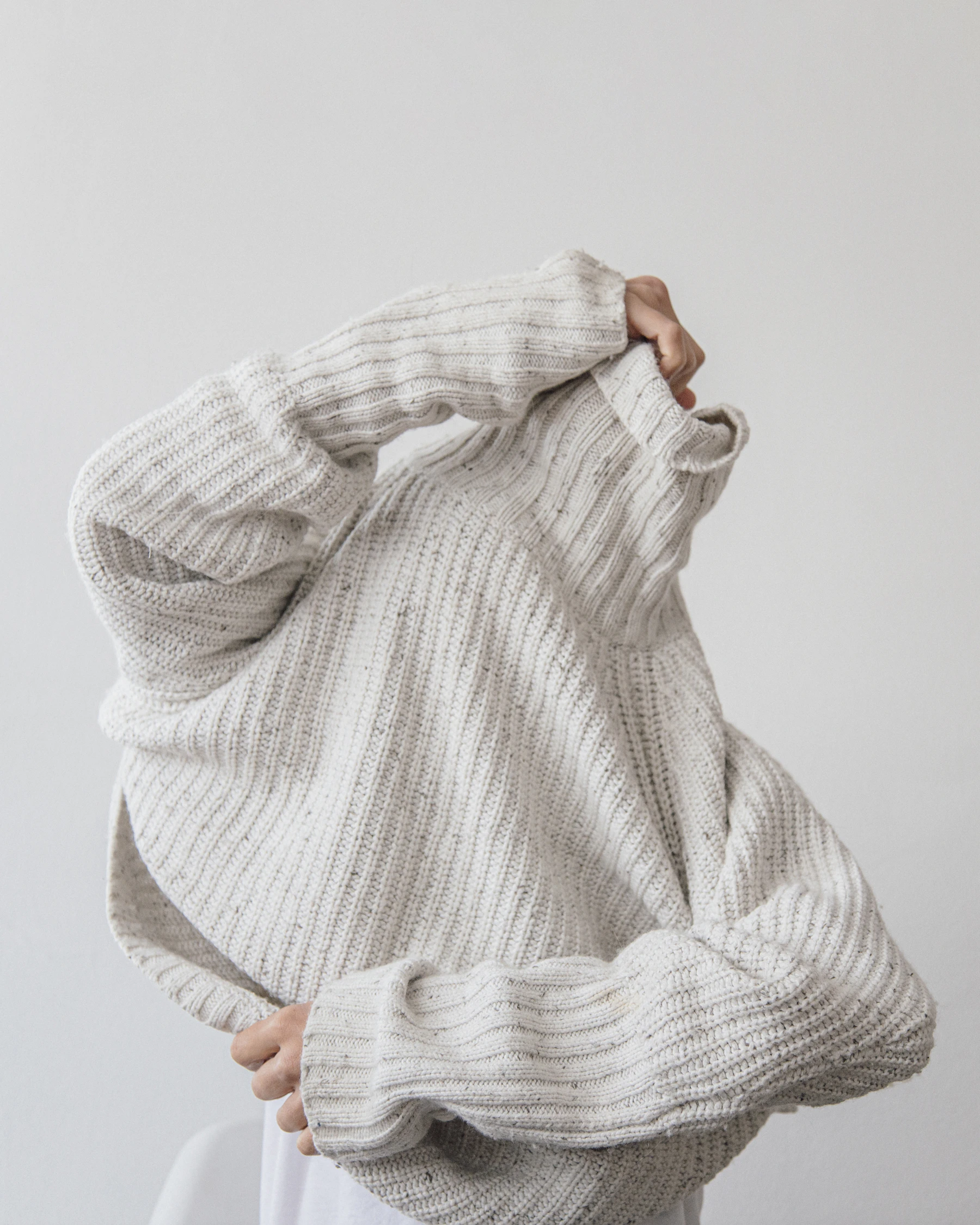 Someone pulling on a chunky cream wool sweater
