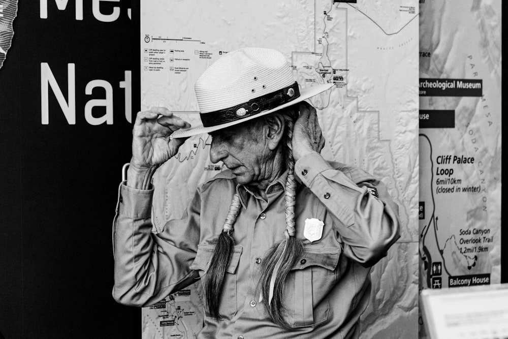 grayscale photography of man with long hair facing his right side while touching hat