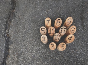 Wooden numbered pegs arranged in a tight cluster on an asphalt surface, each peg displaying a black number from 1 to 12.