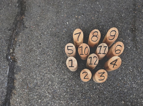 Wooden numbered pegs arranged in a tight cluster on an asphalt surface, each peg displaying a black number from 1 to 12.