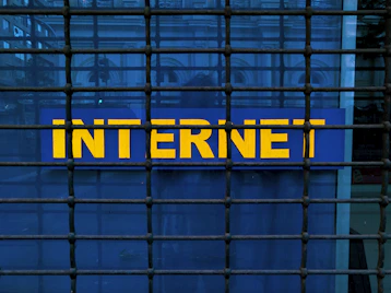 A metal grid covers a blue sign with the word 'INTERNET' written in bold, yellow letters. The grid creates a pattern of squares across the image, adding an element of confinement or security.