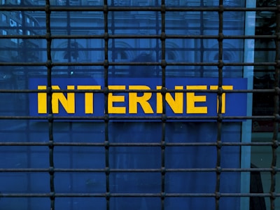 A metal grid covers a blue sign with the word 'INTERNET' written in bold, yellow letters. The grid creates a pattern of squares across the image, adding an element of confinement or security.