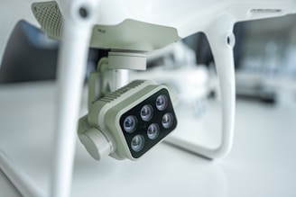 A close-up view of a camera attached to a drone, featuring multiple lenses arranged in a rectangular formation. The setting is likely a laboratory or studio, characterized by minimalist surroundings and a soft light ambience that accentuates the drone's technical components.