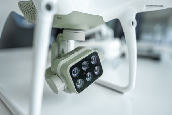 A close-up view of a camera attached to a drone, featuring multiple lenses arranged in a rectangular formation. The setting is likely a laboratory or studio, characterized by minimalist surroundings and a soft light ambience that accentuates the drone's technical components.