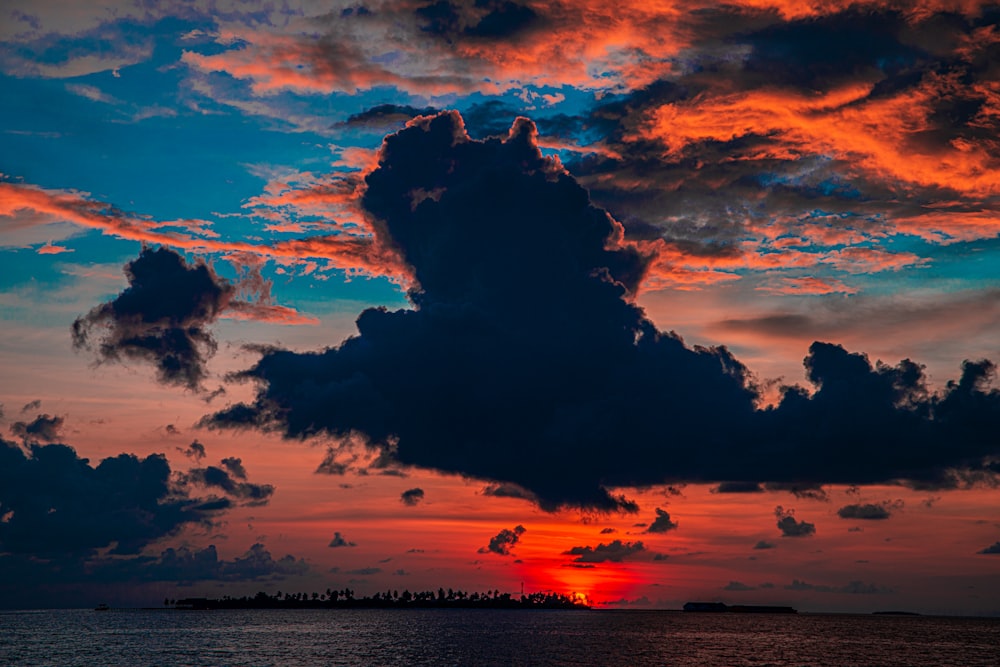 the sun is setting over the ocean with clouds in the sky