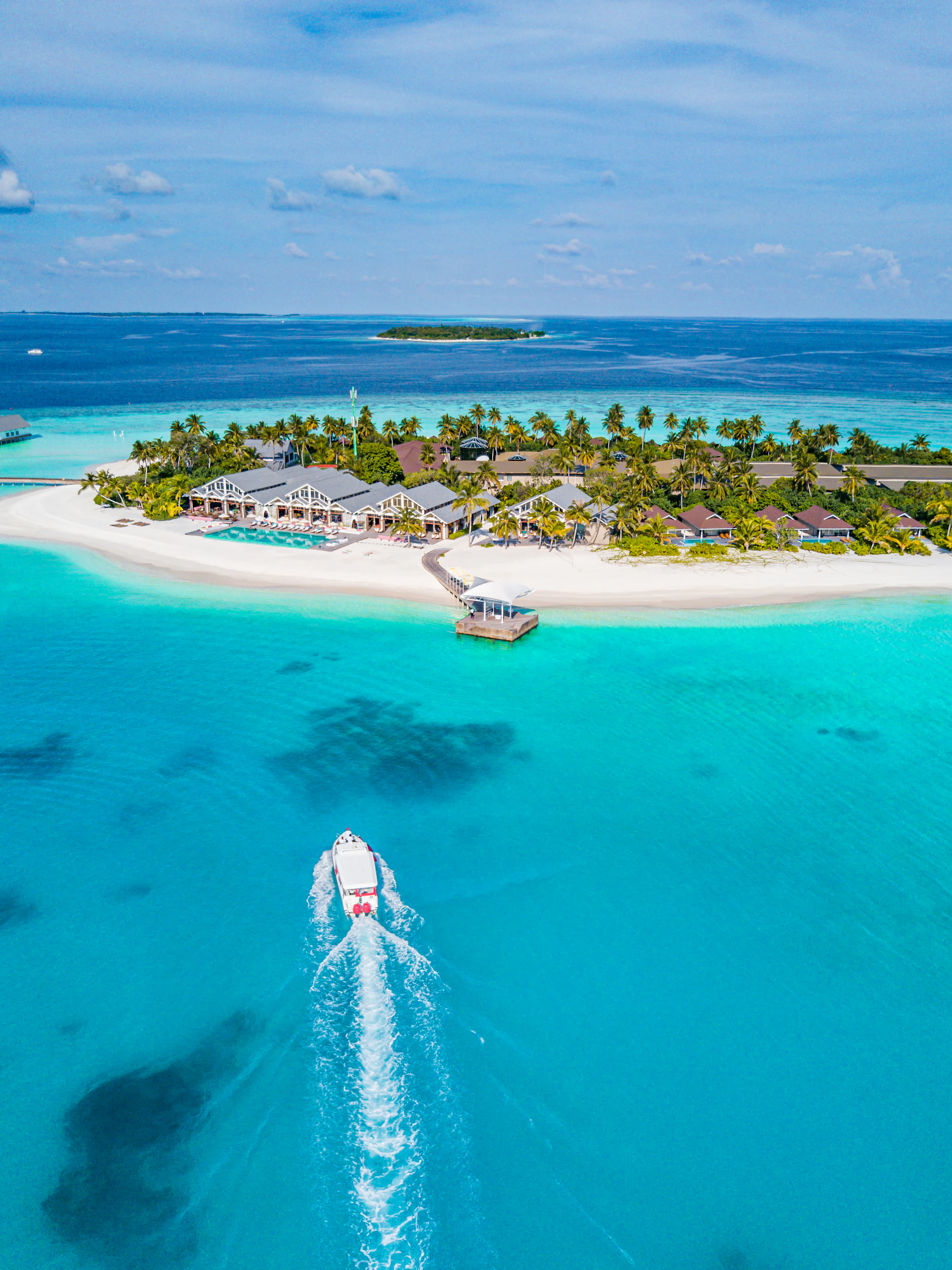 A speedboat trailing a white wake toward a small resort island