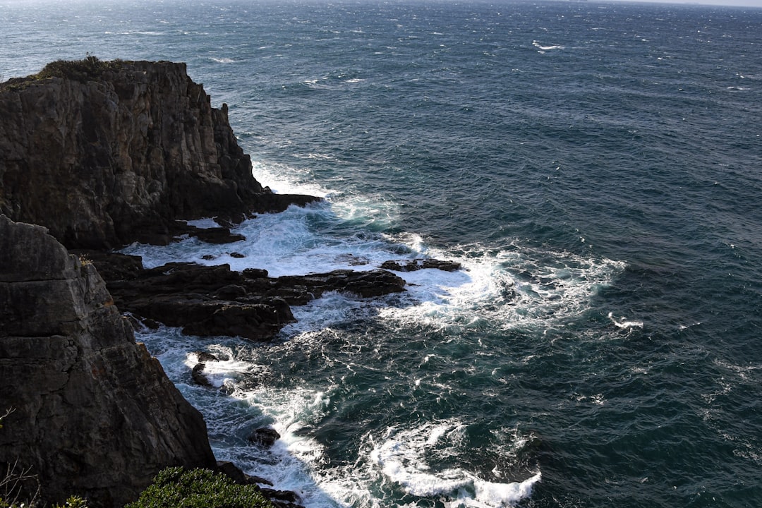 a large body of water next to a rocky cliff,<p></figure>Yoshino-Kumano National Park Sandanbeki Rock Cliffs