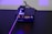 A black electronic device with a digital display showing the number 1.604, surrounded by control buttons. A purple laser beam is emitted from the device, projecting onto a perforated black surface.