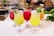 A selection of vibrantly colored tropical cocktails served in elegant glassware, each garnished with fresh mint leaves and decorative skewers. The drinks range in color from yellow to red, showcasing a refreshing appearance. They are placed on a white surface with a blurred background suggesting a bar setting.