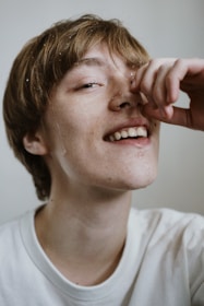 A smiling person washing their face with glamenow facewash, water droplets catching the light.