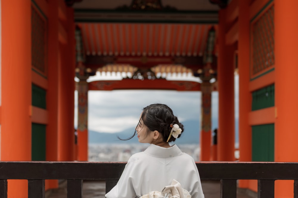 woman wearing white kimono standing while facing back near red building