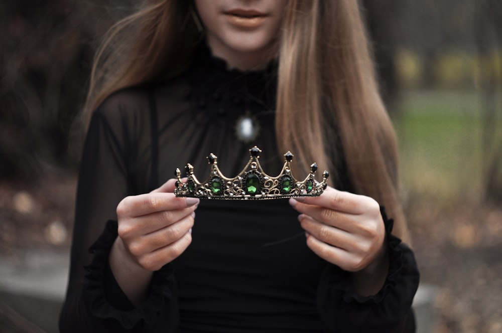 woman wearing black long-sleeved blouse standing while holding green and silver tiara