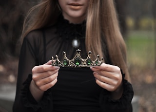 woman wearing black long-sleeved blouse standing while holding green and silver tiara