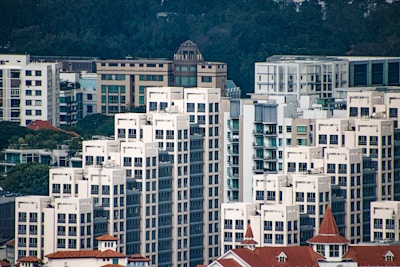 A dense cluster of modern high-rise buildings with varied architectural styles, predominantly featuring white facades and large windows. Some structures have distinct red roofs, set against a backdrop of lush green trees.