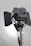 A large professional film or photography studio light with adjustable barn doors and a sturdy metal stand. The light source appears to be positioned against a plain background with soft illumination.