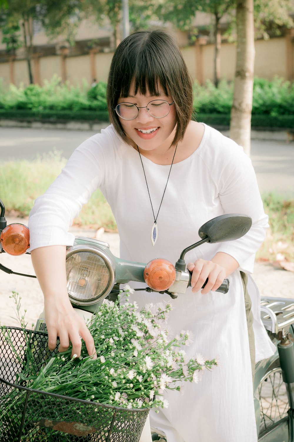 woman wearing white long-sleeved dress putting white flowers in motor scooter sack\