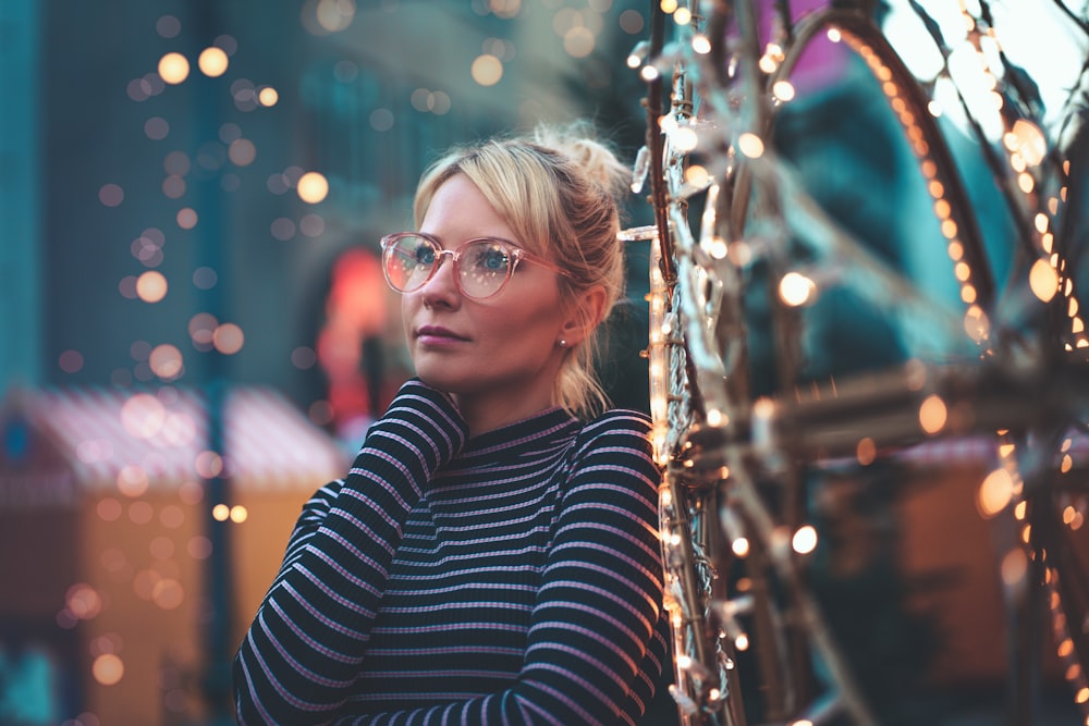 woman wearing black and white striped crew-neck long-sleeved shirt and eyeglasses standing near lighted string lights