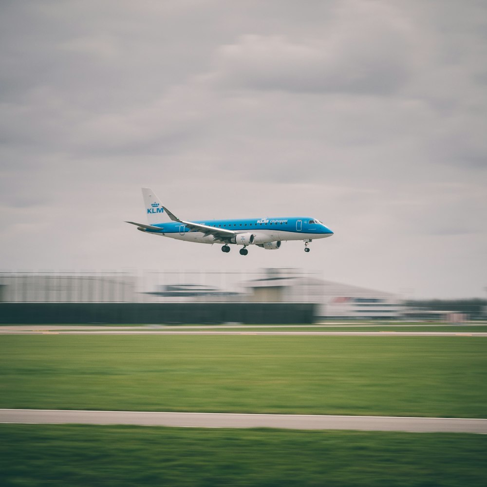 avion de passagers blanc et bleu au-dessus du champ vert sous le ciel blanc