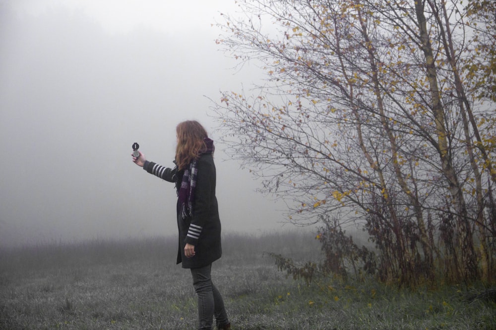 woman wearing black jacket using compass white standing on green field in foggy day