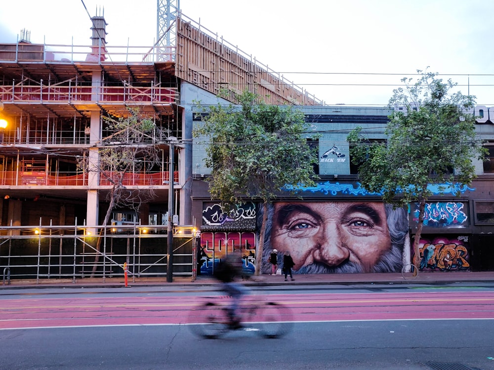 person biking on road near multicolored graffiti art on building