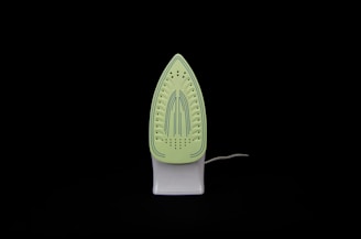 An iron is placed upright against a black background. The soleplate is visible and has a light green color with blue stripe details and multiple steam holes.