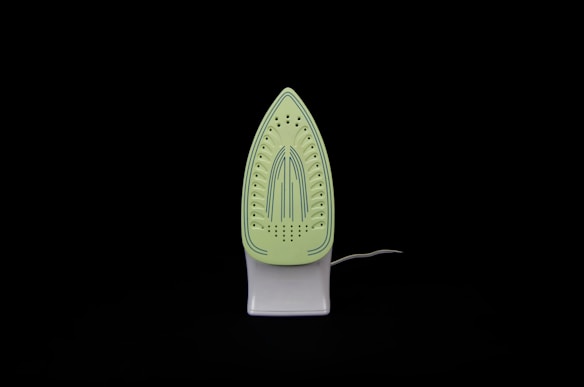An iron is placed upright against a black background. The soleplate is visible and has a light green color with blue stripe details and multiple steam holes.