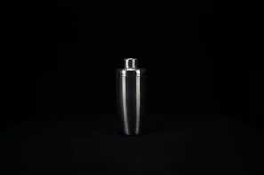 Close-up of a sleek stainless steel cocktail shaker catching soft light on a deep teal background