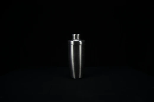 A sleek, polished stainless steel cocktail shaker resting on a crisp white marble countertop with soft teal accents in the background.