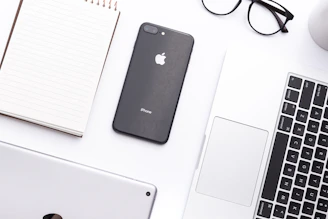 A bright, minimalist workspace featuring a laptop, smartphone, and stylish everyday items arranged neatly.