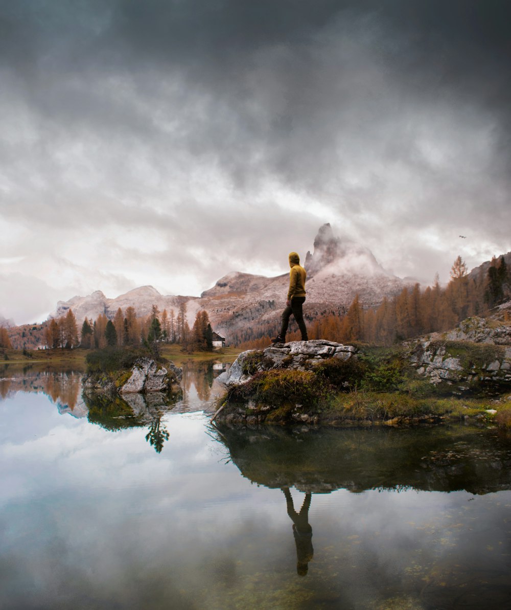 man standing on stone near calm body of water