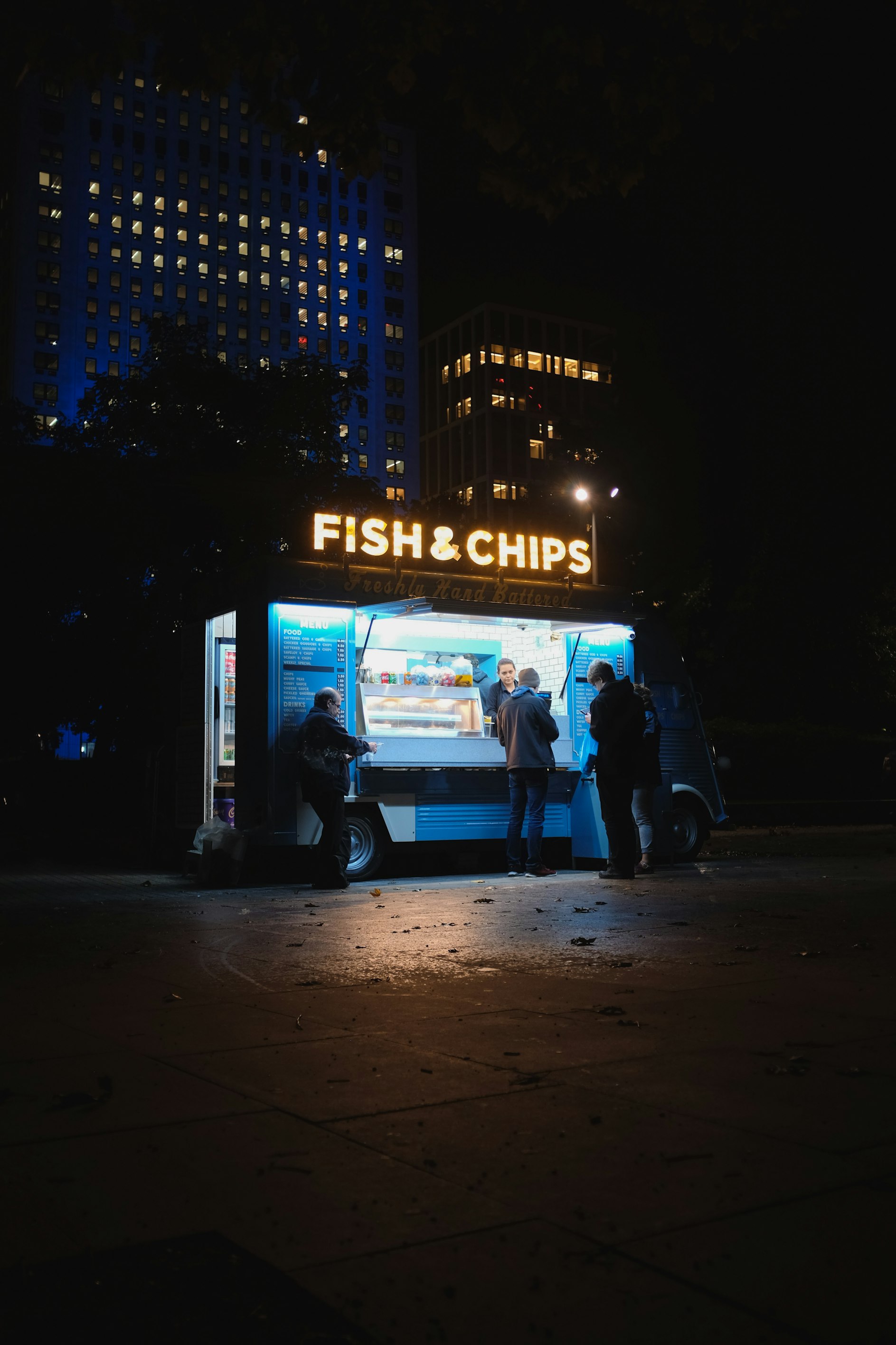 3 shadowy figures at a fish and chip van at night