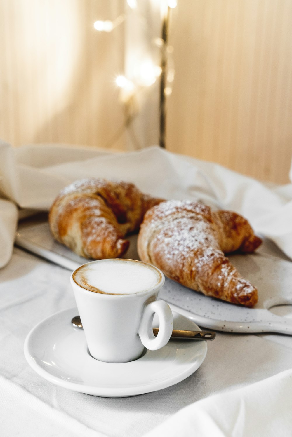 white teacup beside tray of croissant
