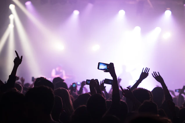 A friendly customer texting on their phone while holding event tickets with a lively concert crowd in the background.