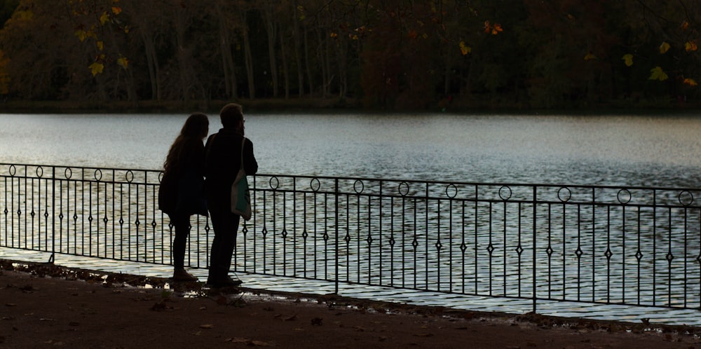 silhouette photo of man and woman beside lake